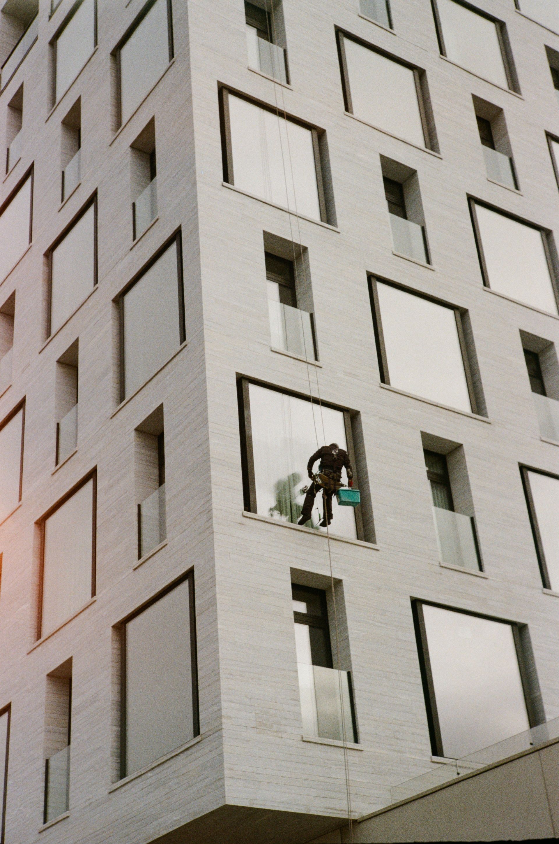 Window cleaner scaling a modern building exterior in daylight.